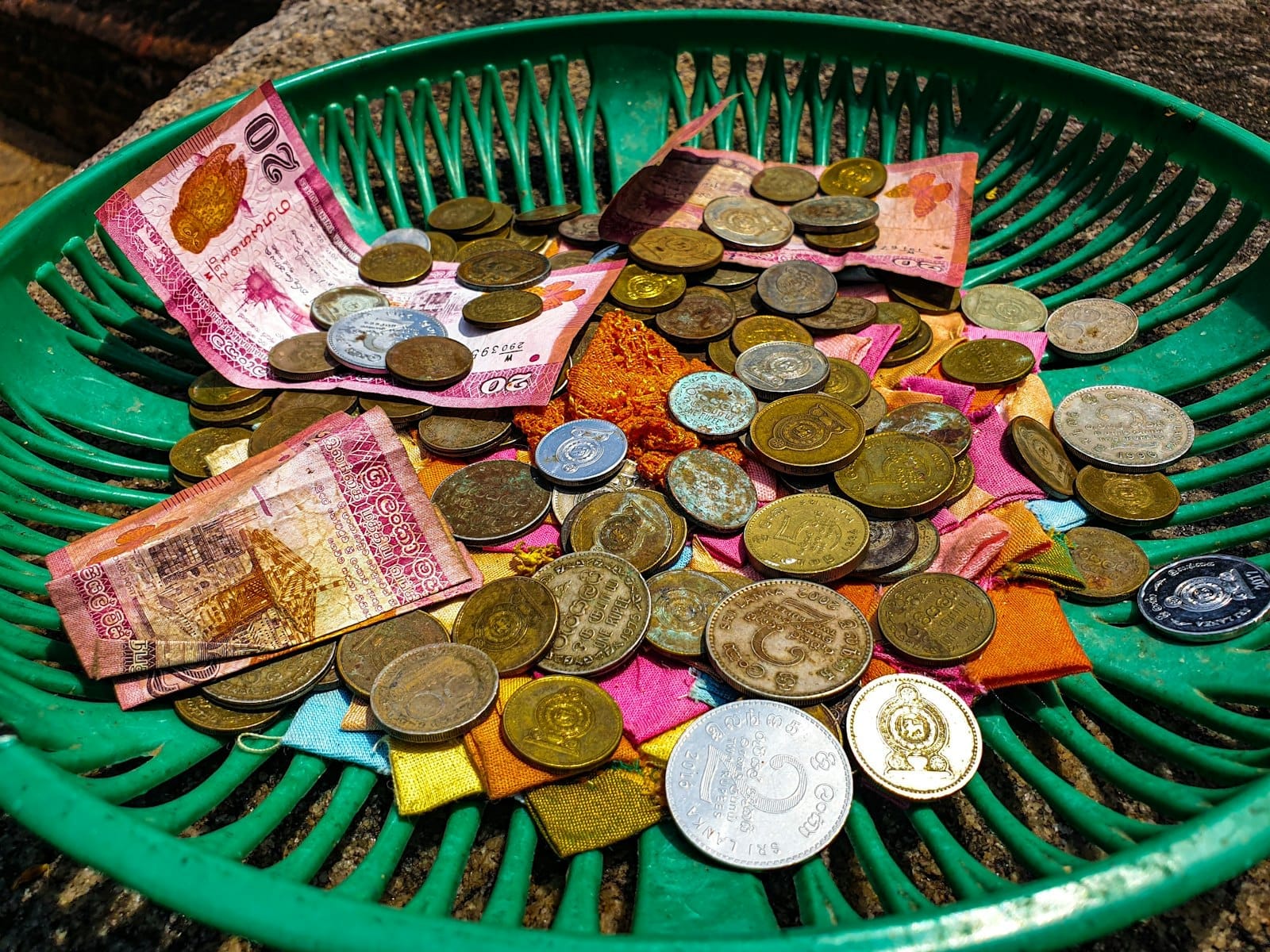 Primer plano de monedas y billetes de baht tailandés en una cesta verde, con luz solar que resalta la moneda local comúnmente utilizada en Chiang Mai.