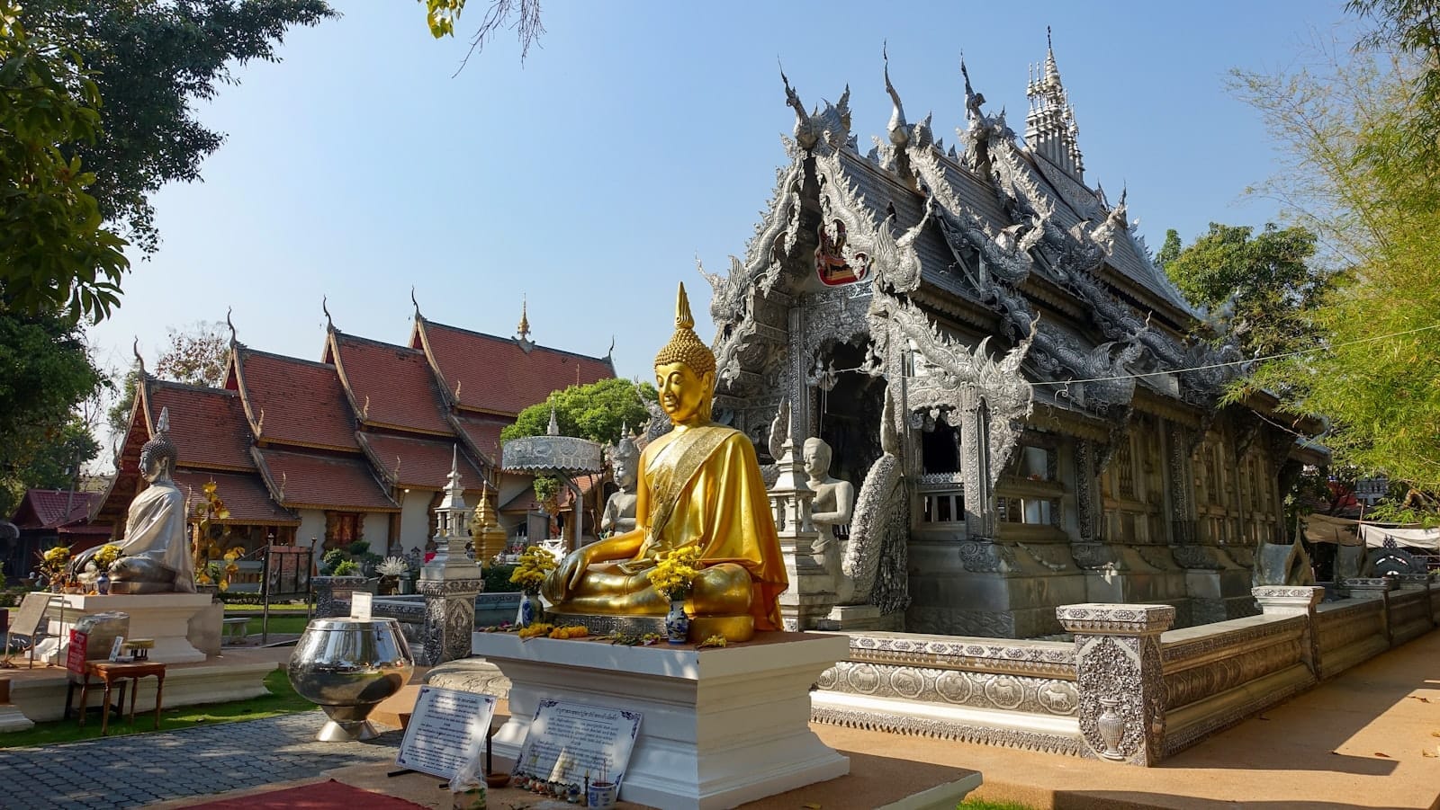 Estatua dorada de Buda y ornamentado templo de plata en Wat Sri Suphan en Chiang Mai bajo un sol despejado.