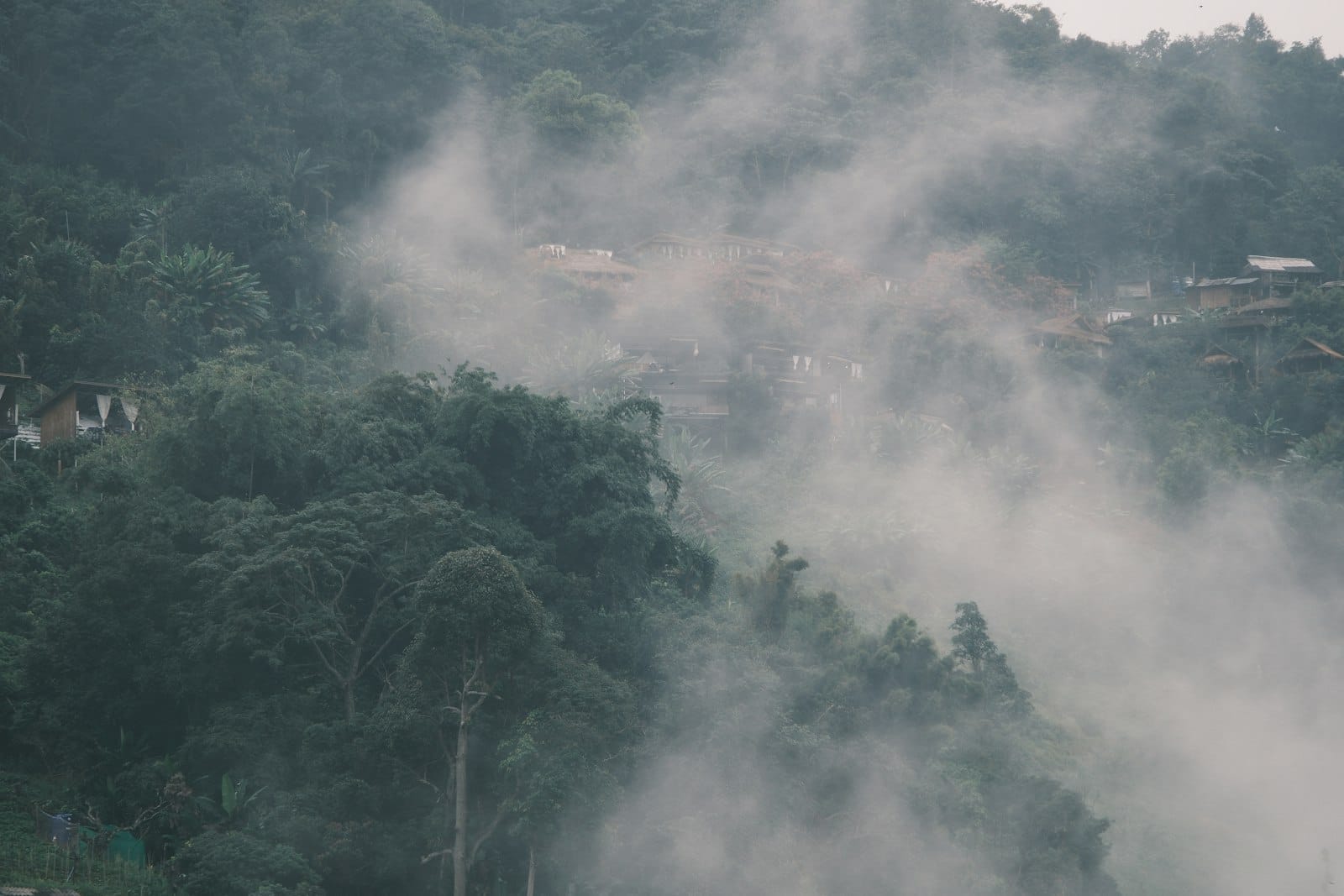 Niebla y neblina cubren una ladera boscosa con tenues señales de asentamiento rural, ilustrando los problemas de calidad del aire cerca de Chiang Mai.