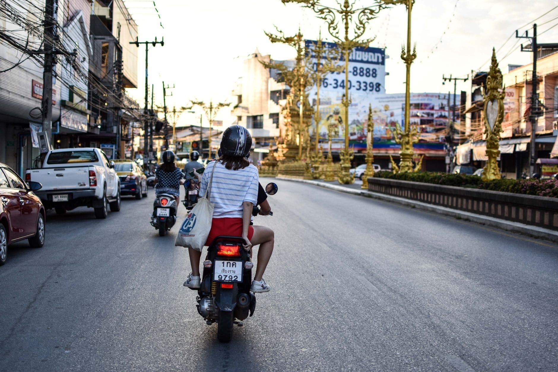 Scooters y motocicletas circulando hacia la famosa torre del reloj dorada de Chiang Rai en una animada escena de calle urbana.