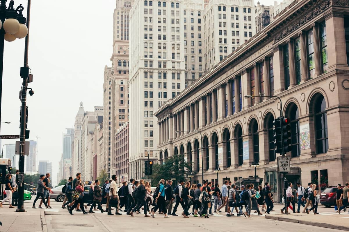 Menschenmassen überqueren eine belebte Kreuzung an der North Michigan Avenue, umgeben von historischen und modernen Wolkenkratzern in der Innenstadt von Chicago.