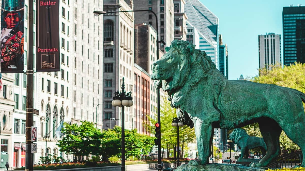Ikonische Bronzelöwenstatue vor dem Art Institute of Chicago mit der Michigan Avenue und historischer Architektur im Hintergrund.