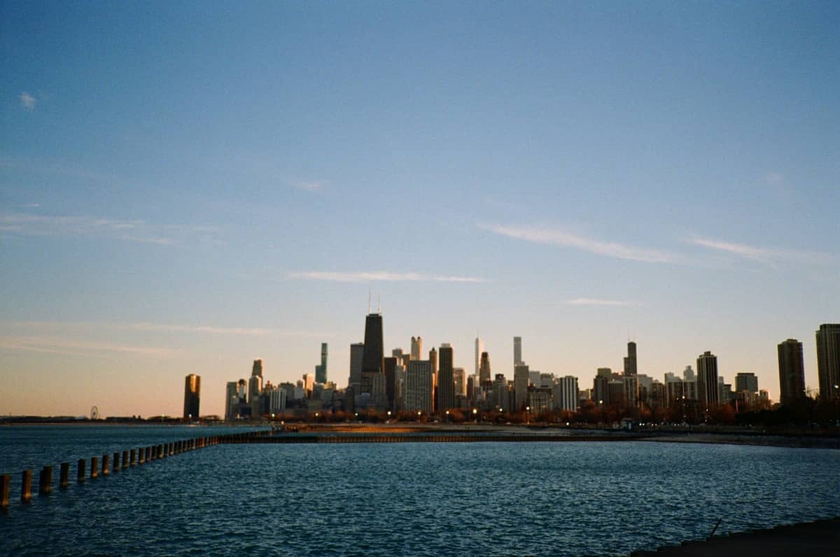 Frente al lago de Chicago al anochecer con una vista clara del skyline de la ciudad, el paseo marítimo suavemente iluminado y agua tranquila en primer plano.