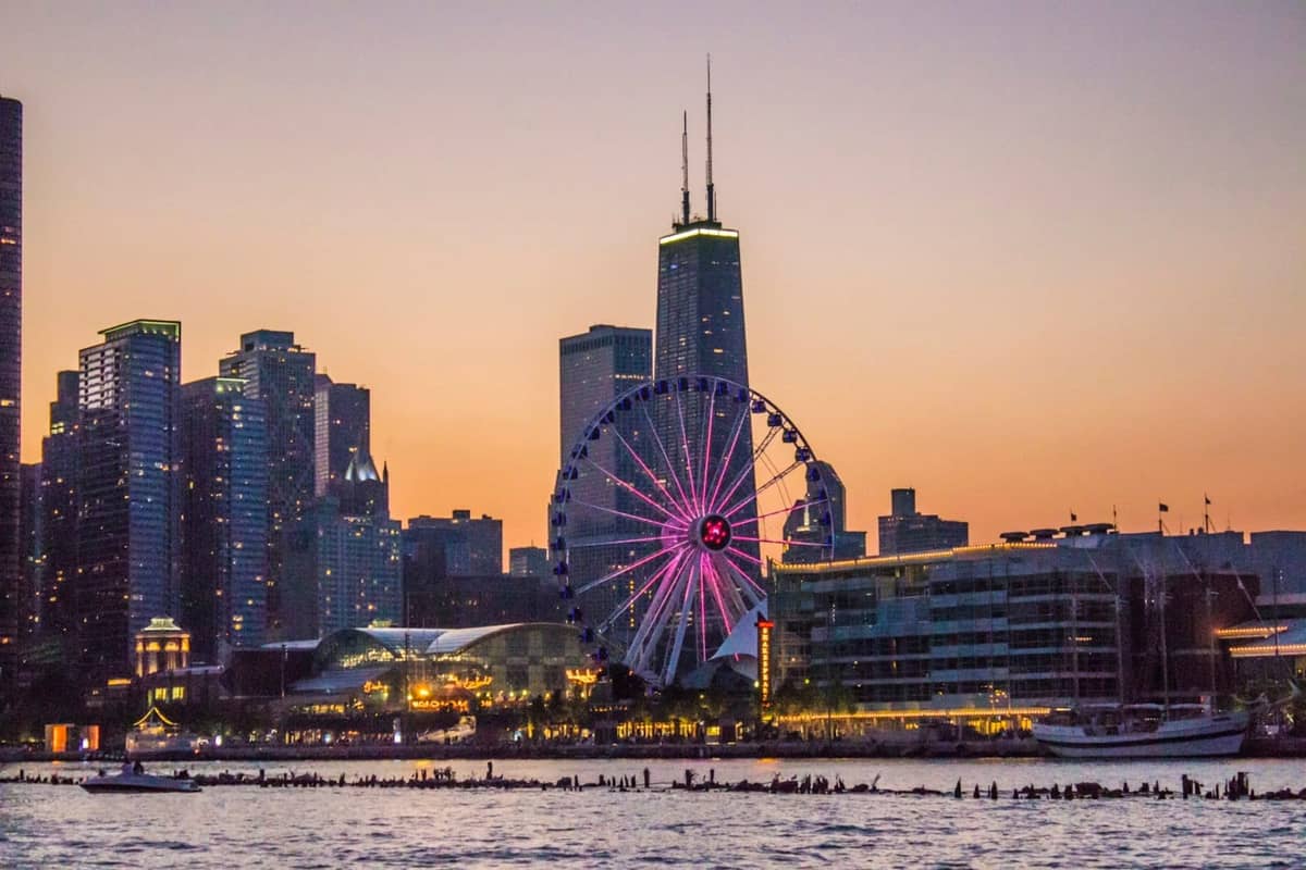 La noria de Navy Pier iluminada al atardecer con el horizonte de Chicago y el agua en primer plano.