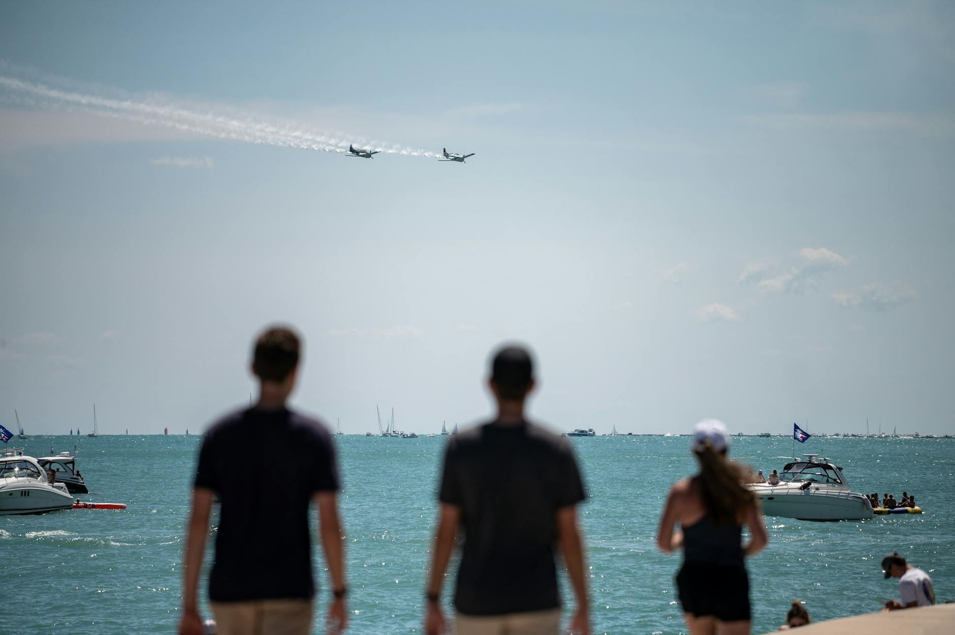 La folla sul lungolago di Chicago osserva i jet mentre eseguono acrobazie aeree sul Lake Michigan, con barche sull'acqua in una giornata di sole.