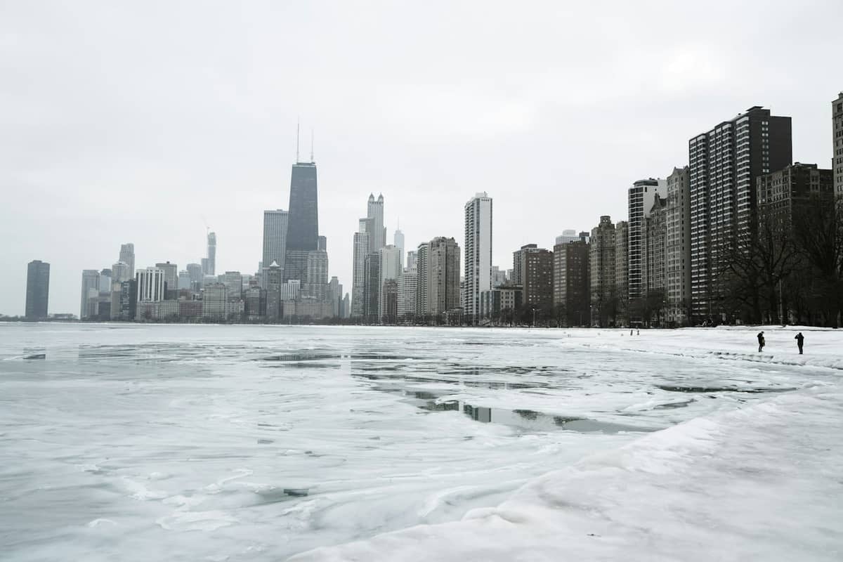 Panorama Chicago z wieżowcami obok zamarzniętego, pokrytego śniegiem jeziora Michigan zimą. Zachmurzone niebo i lodowy krajobraz dominują w scenie.