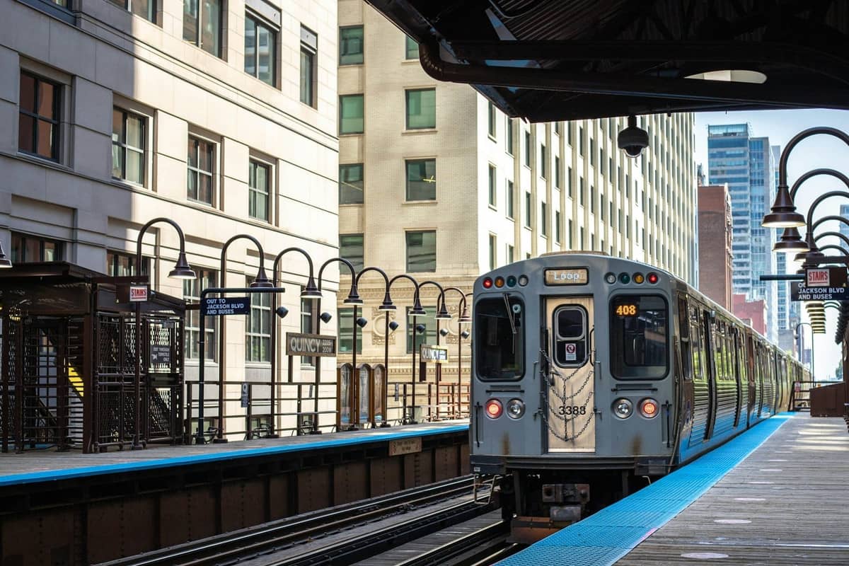 Pociąg nadziemny 'L' w Chicago przyjeżdżający na nadziemny peron w centrum otoczony wysokimi budynkami w pogodny dzień.