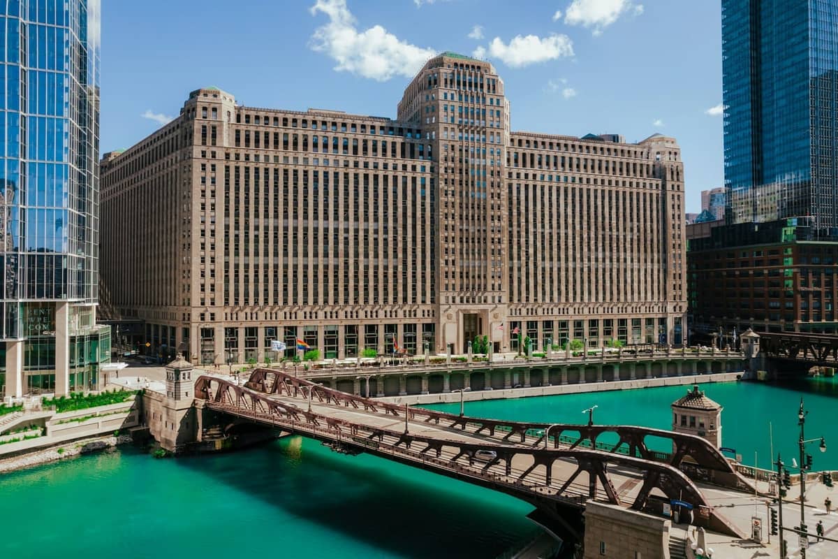 The Merchandise Mart building on the Chicago River, with a bridge and turquoise water in the foreground under a blue sky.