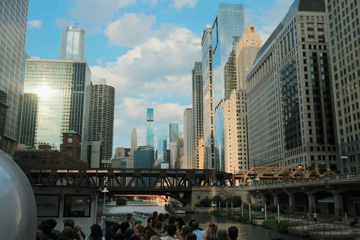 Tour boat filled with people cruising the Chicago River, surrounded by iconic downtown skyscrapers on a sunny day.