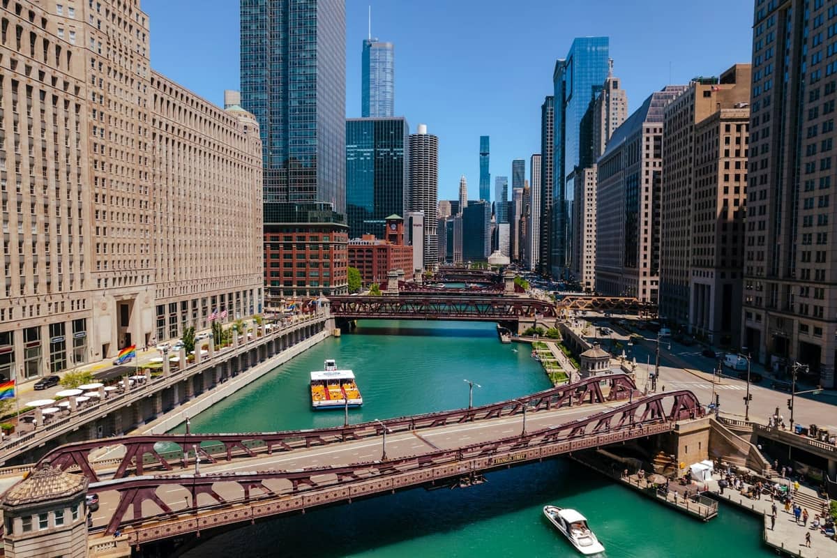 A vibrant view of boats cruising the Chicago River surrounded by skyscrapers and iconic downtown architecture on a sunny day.