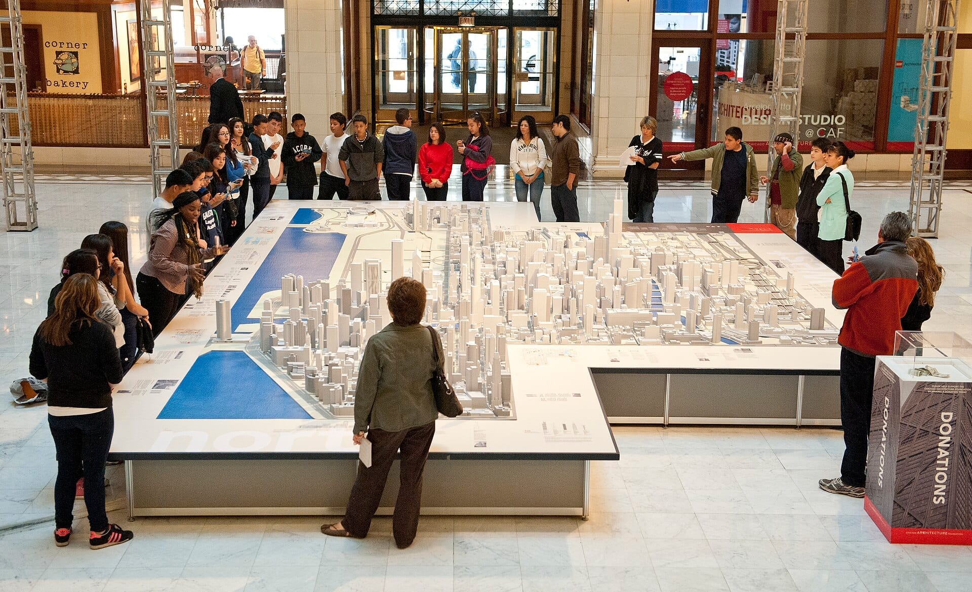 I visitatori si radunano intorno a un intricato plastico in scala di Chicago presso il Chicago Architecture Center, con la luce naturale che illumina la spaziosa sala espositiva.