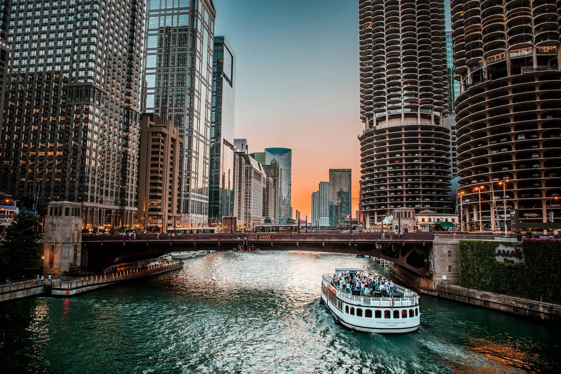 Un battello del Chicago River Cruise risale il fiume al tramonto, circondato dagli iconici grattacieli del centro e dai ponti della città sotto un cielo luminoso.