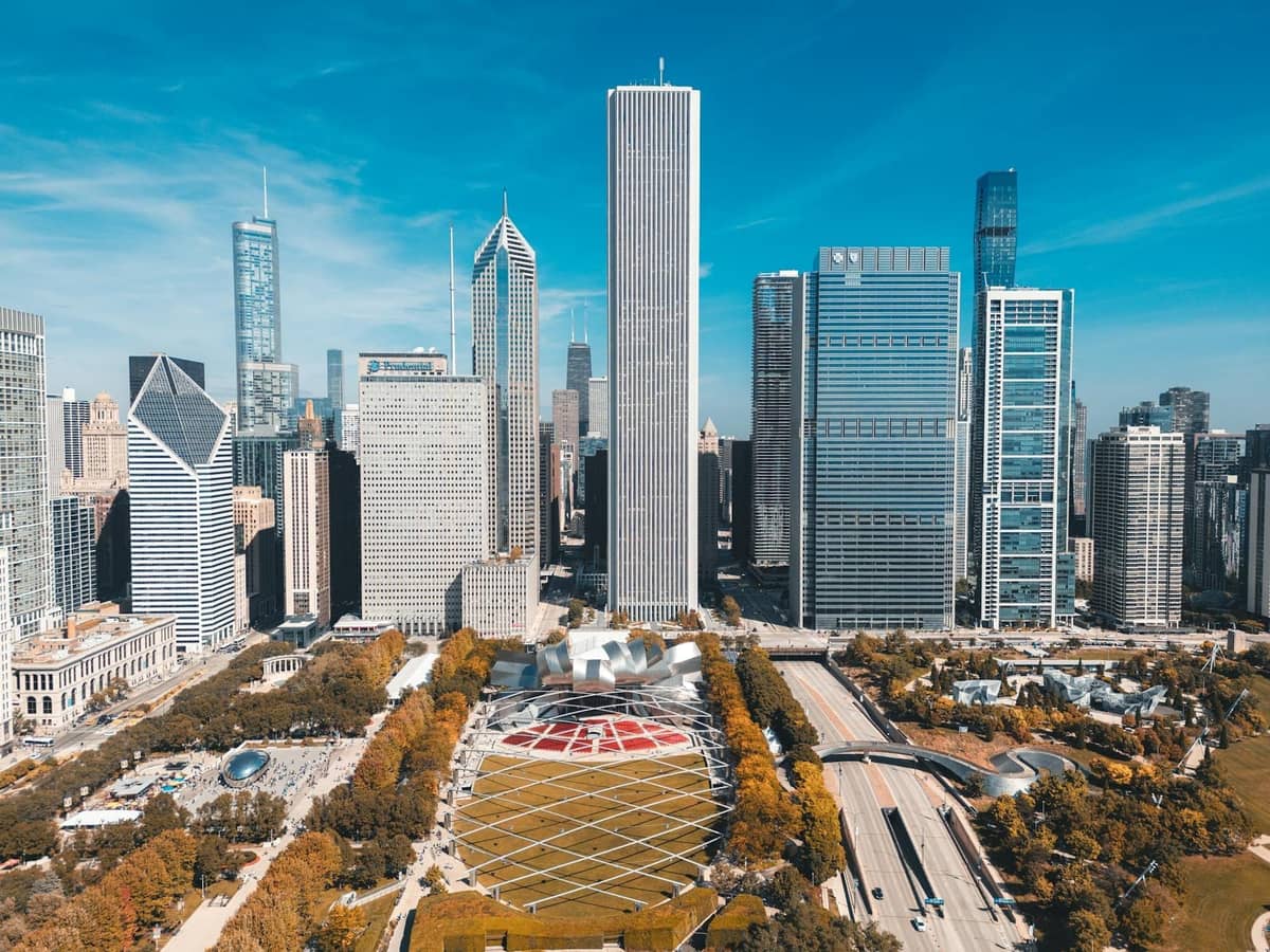 Aerial view of downtown Chicago with prominent modern skyscrapers and Pritzker Pavilion's curving structure in Millennium Park on a clear day.