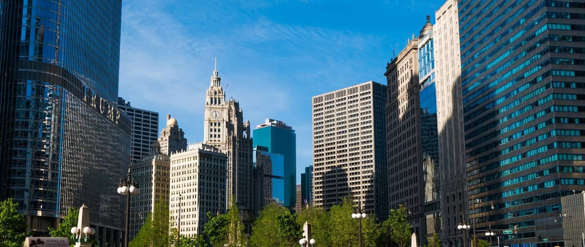 Daytime view of Chicago Riverfront with Wrigley Building, Tribune Tower, and modern skyscrapers against a clear blue sky.