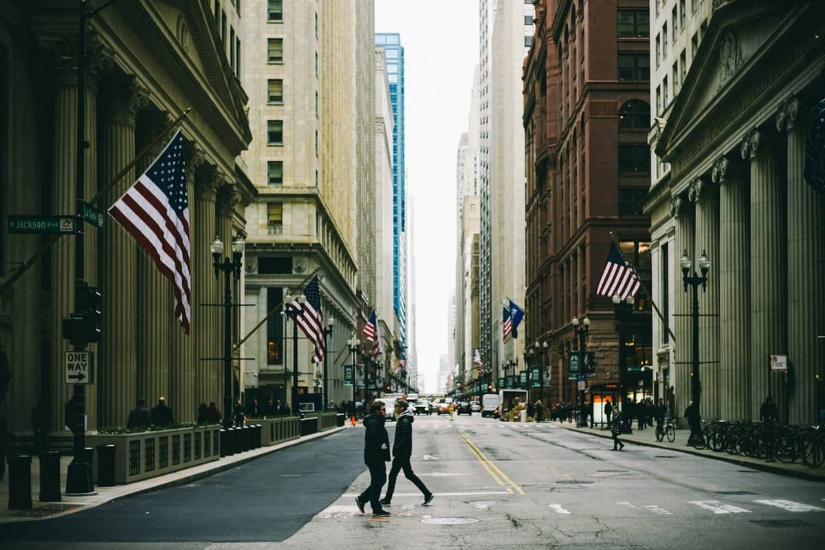 Street view in Chicago's Loop showing historic buildings with columns, American flags, and people crossing at the intersection of LaSalle and Dearborn.