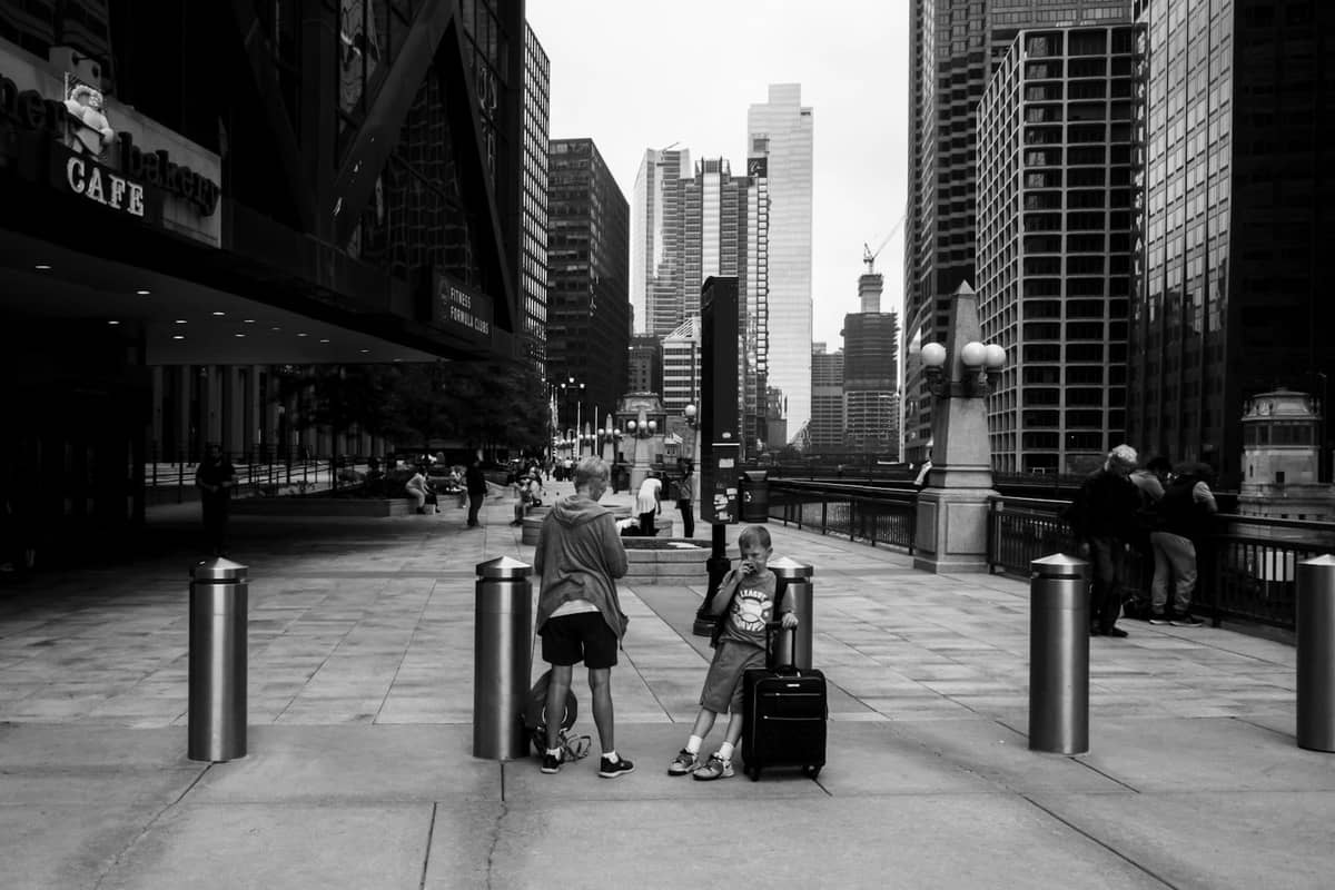 Street scene in downtown Chicago with people near luggage, skyscrapers, and architecture along the riverwalk.