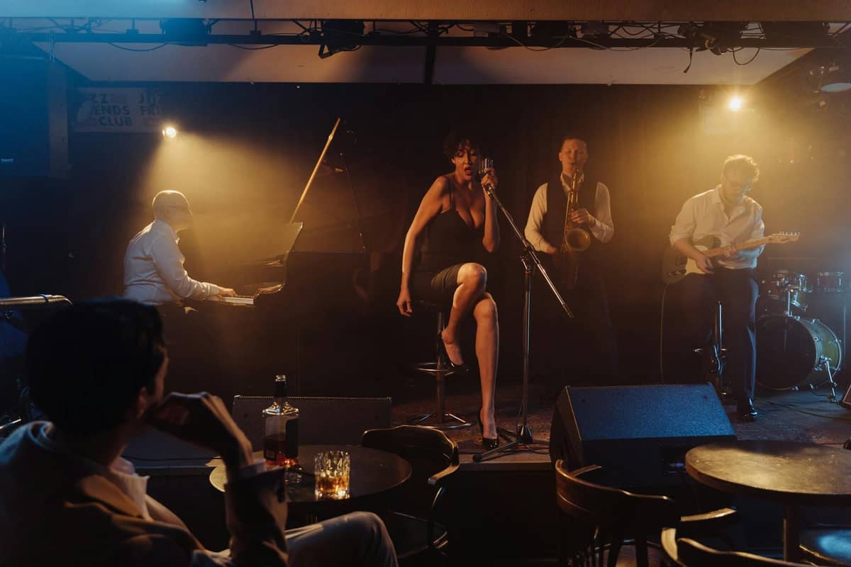 Jazzband, die live auf einer schwach beleuchteten Bühne in einem Club mit Tischen und Getränken im Vordergrund auftritt.