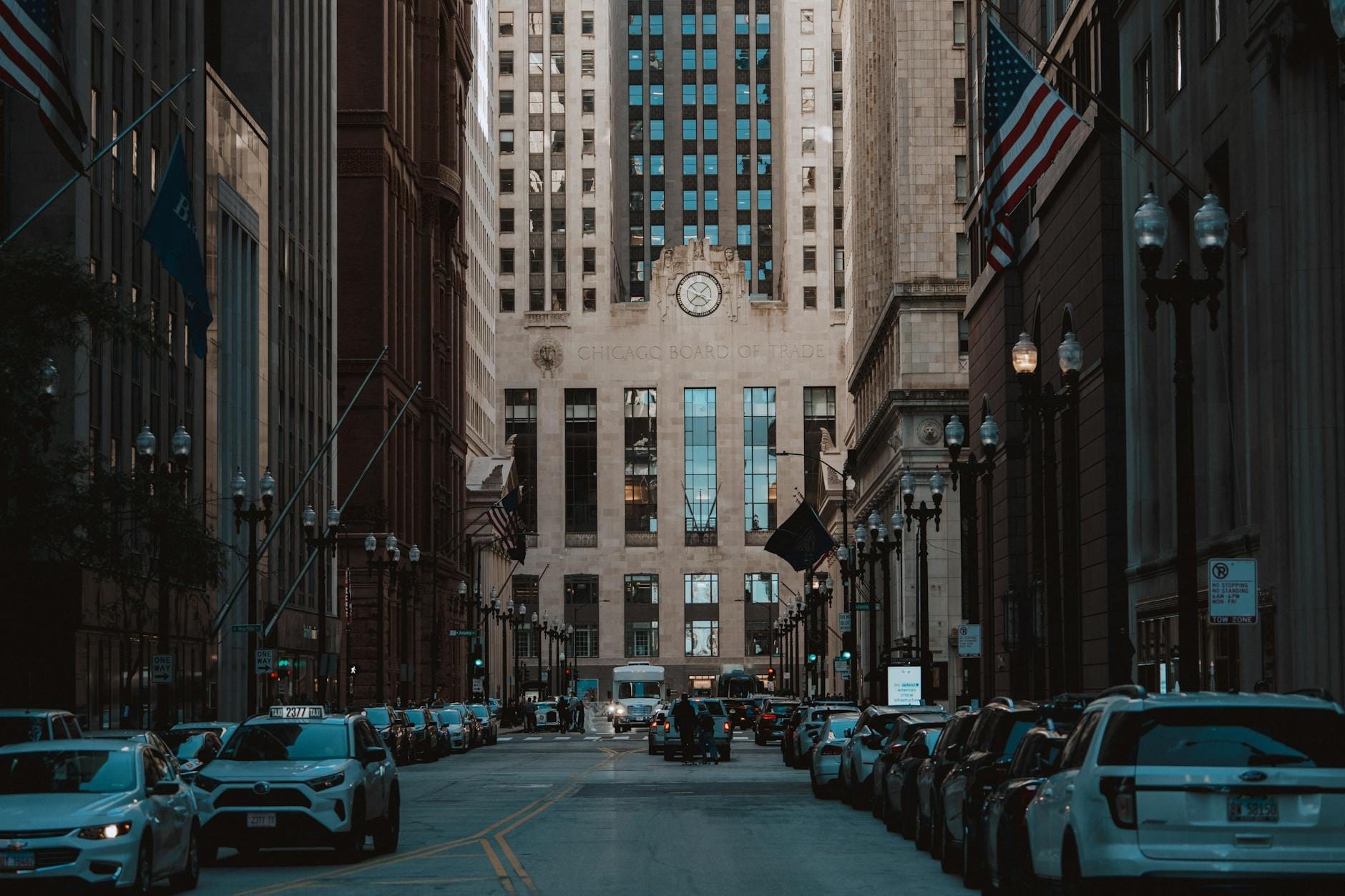 Vista dal basso del Chicago Board of Trade Building incorniciato da grattacieli e bandiere americane, con le auto parcheggiate lungo LaSalle Street nel centro di Chicago.