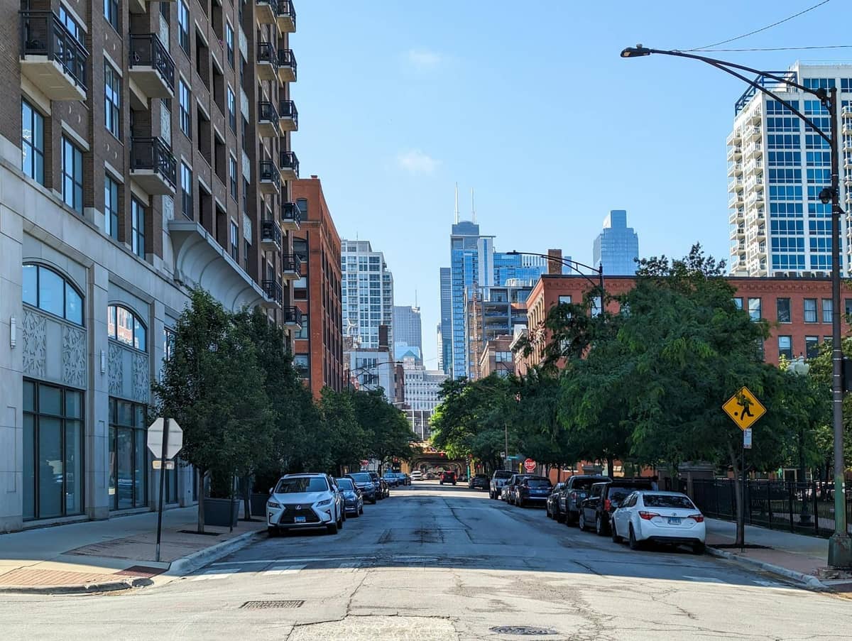 Baumgesäumte Straße in Chicago mit geparkten Autos, Backsteinapartments und der Skyline der Stadt in der Ferne an einem sonnigen Tag.
