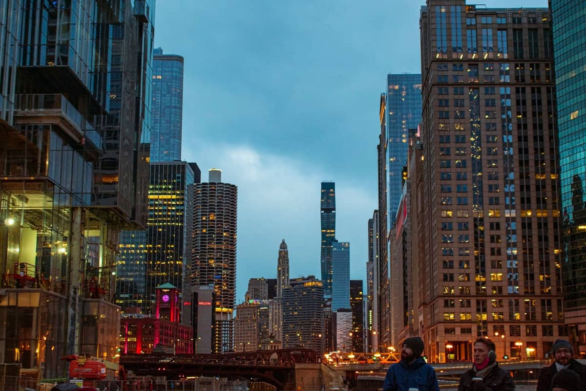 Paisaje urbano del centro de Chicago al atardecer con rascacielos iluminados, el río y personas caminando por una animada calle urbana.
