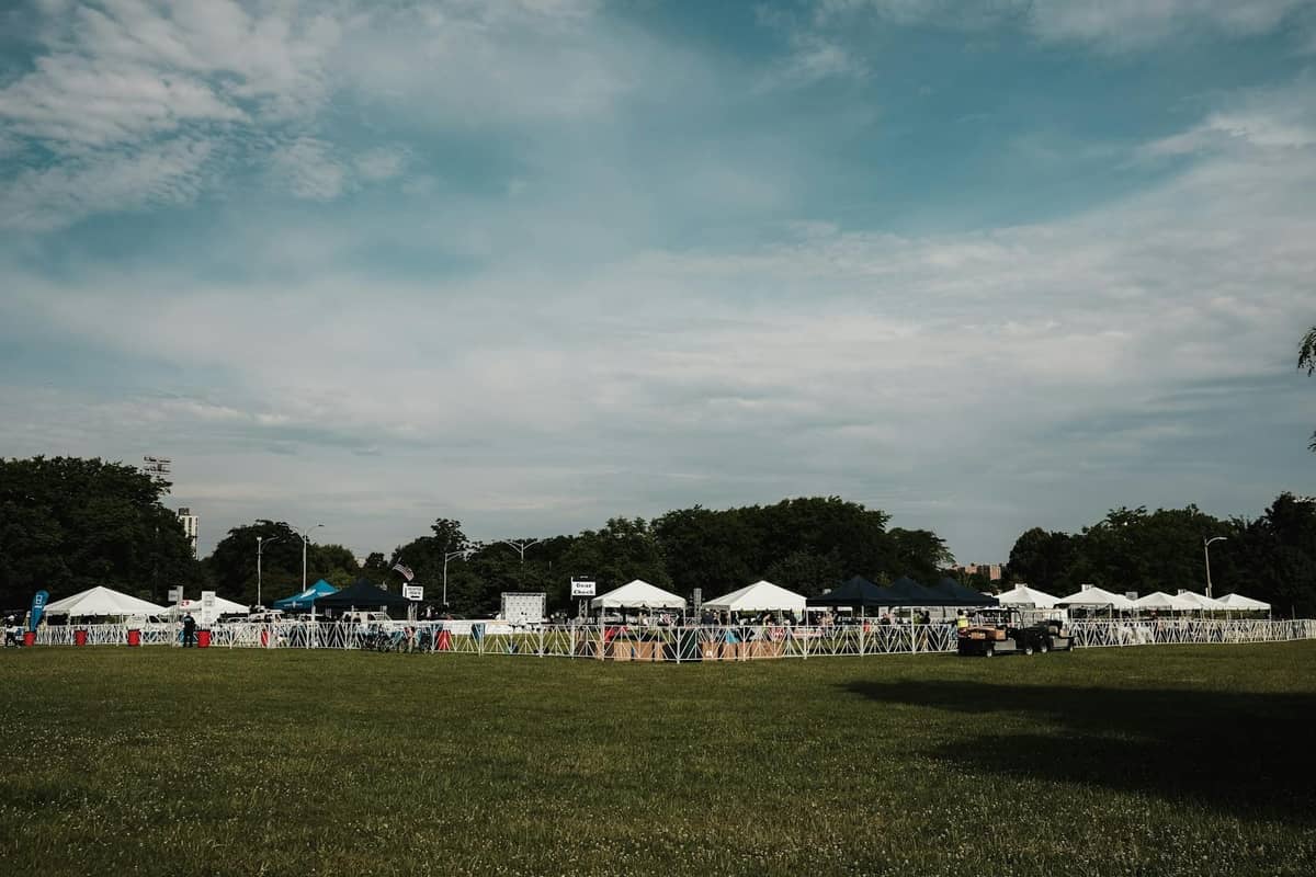 Filas de carpas blancas de festival instaladas en un campo de hierba con personas caminando, bajo cielos azules; escena típica en los festivales gastronómicos al aire libre en Chicago.