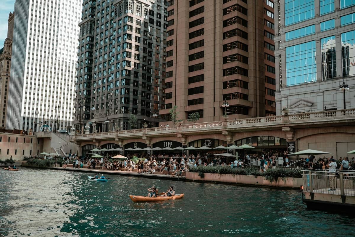 Chicago Riverwalk par une journée ensoleillée avec des personnes dînant sur des terrasses au bord de l'eau et des kayakistes sur la rivière, grands immeubles en arrière-plan.
