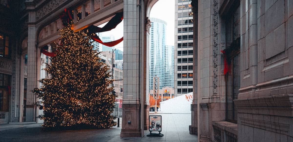 Großer geschmückter Weihnachtsbaum mit Lichtern unter einem verzierten Torbogen in der Innenstadt von Chicago umgeben von hohen Stadtgebäuden.