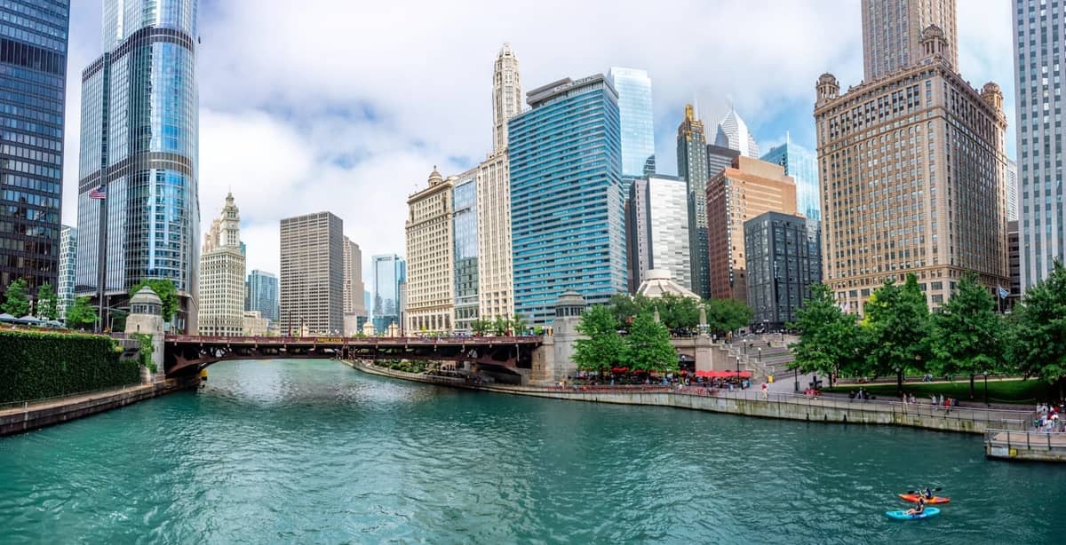 Vista panorámica del Chicago River con el horizonte del centro y un kayakista remando en el agua bajo un cielo azul.