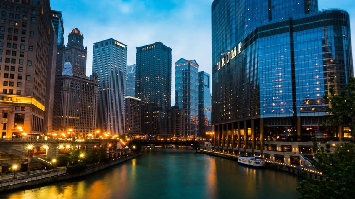Die Chicago Riverwalk in der Abenddämmerung mit Luxushotels und modernen Wolkenkratzern, darunter der Trump Tower, der sich im Wasser spiegelt.