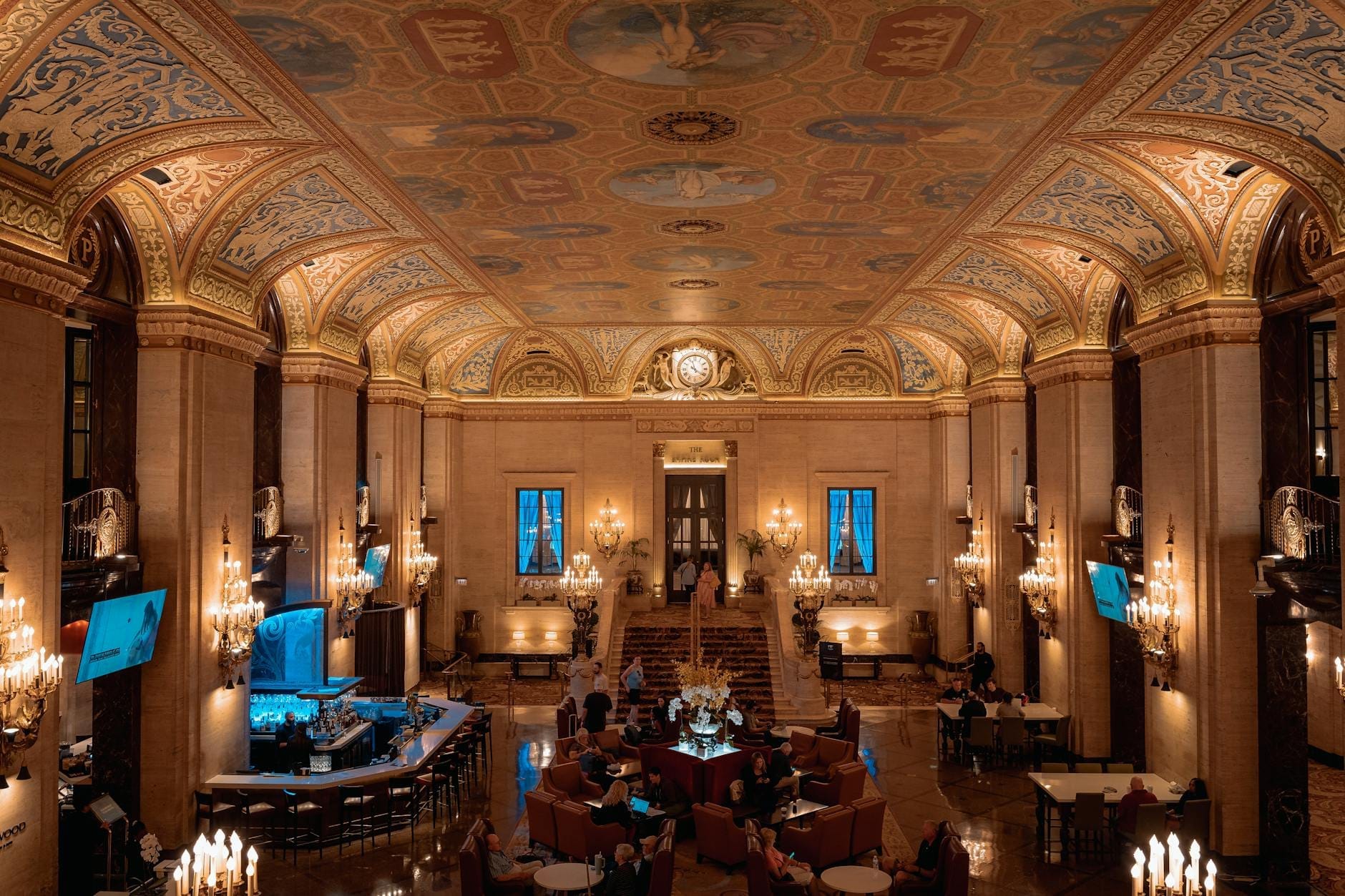 Saguão grandioso de um hotel de luxo em Chicago com tetos pintados ornamentados, lustres elegantes e hóspedes relaxando em poltronas sofisticadas.