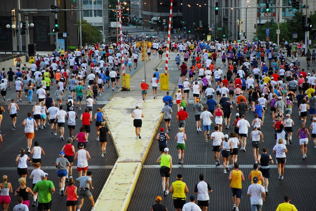 A large group of runners participating in a marathon crosses a city bridge with downtown Chicago buildings in the background.