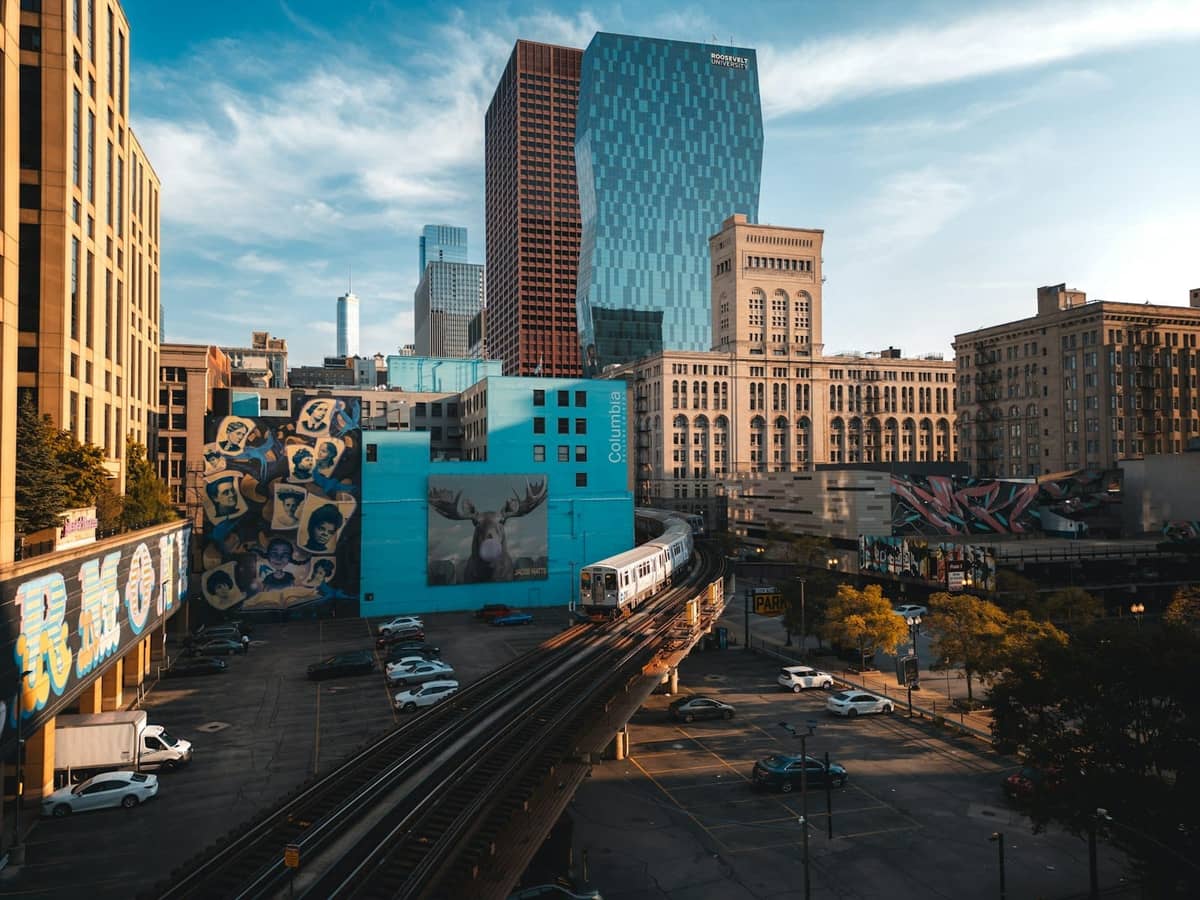 Vista del treno sopraelevato di Chicago che attraversa il South Side con alti edifici moderni, murales urbani e una strada cittadina illuminata dal sole.