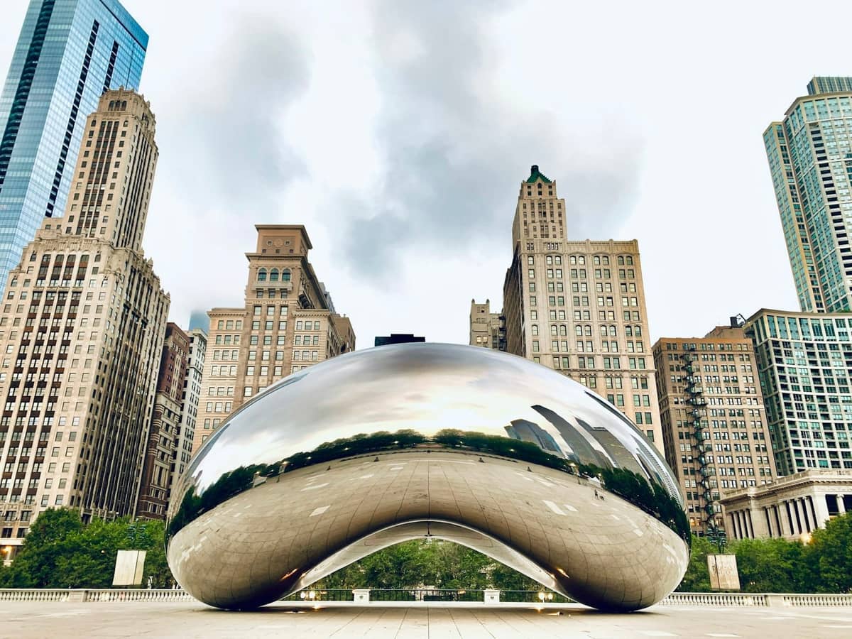 Scultura Cloud Gate nel Millennium Park, Chicago, con i grattacieli circostanti e cielo sereno sullo sfondo.
