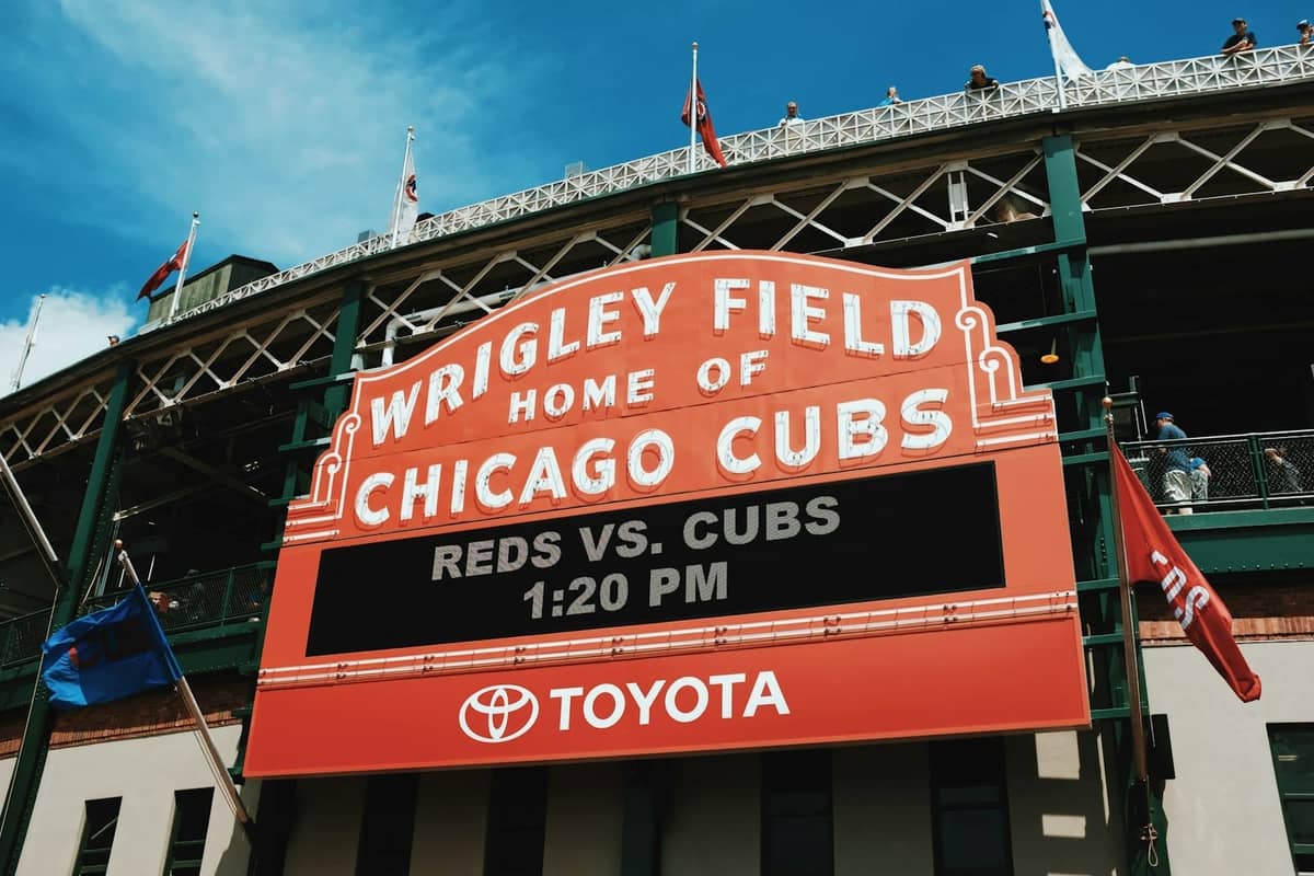L'iconica insegna rossa del Wrigley Field a Chicago, con la scritta Wrigley Field Home of Chicago Cubs, e persone visibili sul tetto.