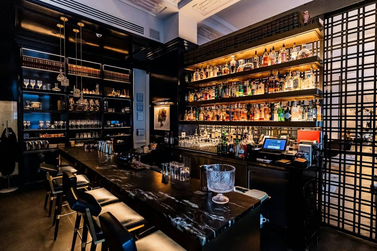 Interno elegante di un bar con scaffali retroilluminati di bottiglie di liquori, piano in marmo e sgabelli moderni in un locale raffinato a Chicago.