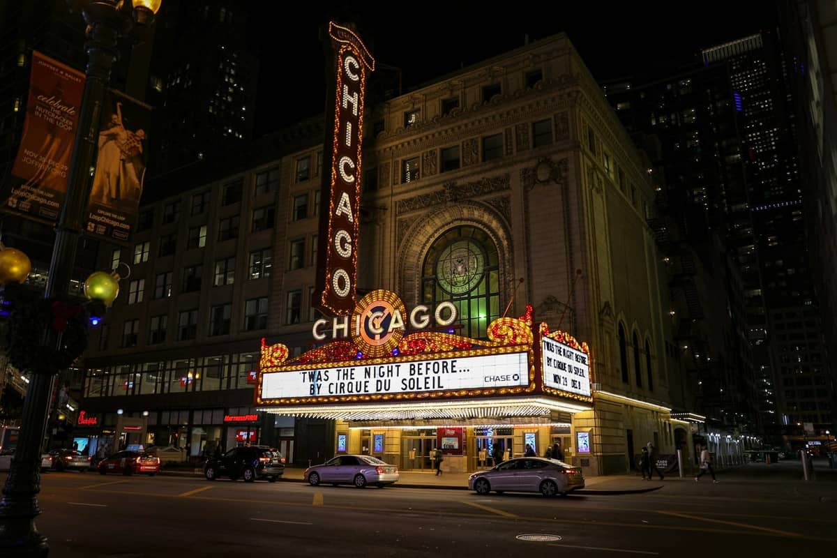 L'iconica insegna del Chicago Theatre illuminata di notte con auto parcheggiate lungo la strada e persone che camminano nelle vicinanze.
