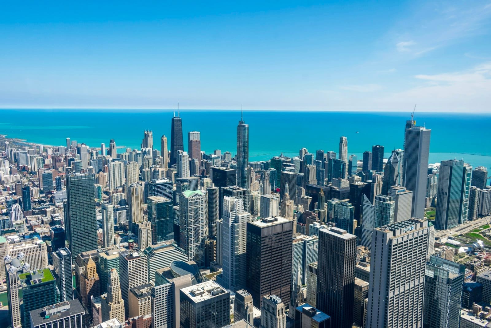 Vista aérea diurna e ensolarada dos arranha-céus do centro de Chicago com o Lago Michigan ao fundo, vista de um mirante elevado.
