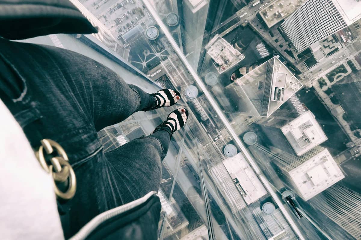 Eine Person steht auf einem Glasvorsprung hoch über Chicago und blickt durch den transparenten Boden direkt nach unten auf die Wolkenkratzer der Stadt.