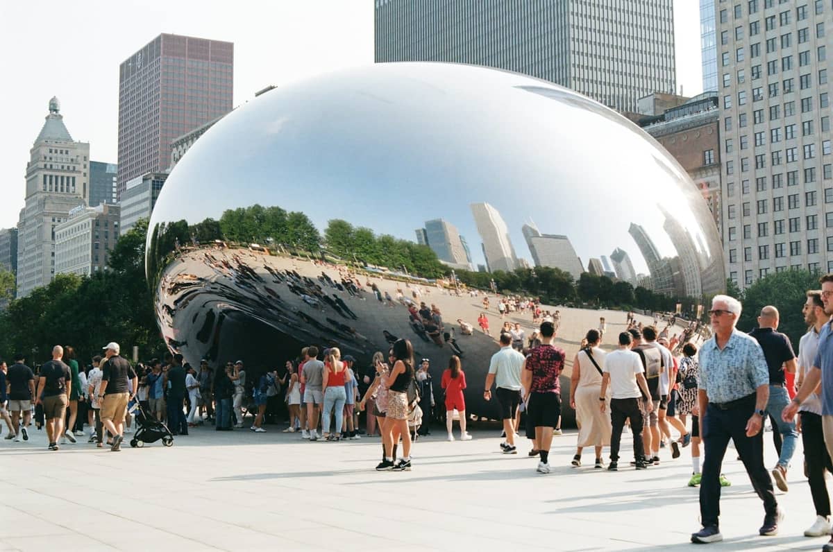 Menschenmassen versammeln sich am Cloud Gate (The Bean) im Millennium Park mit den Wolkenkratzern Chicagos im Hintergrund an einem sonnigen Tag.