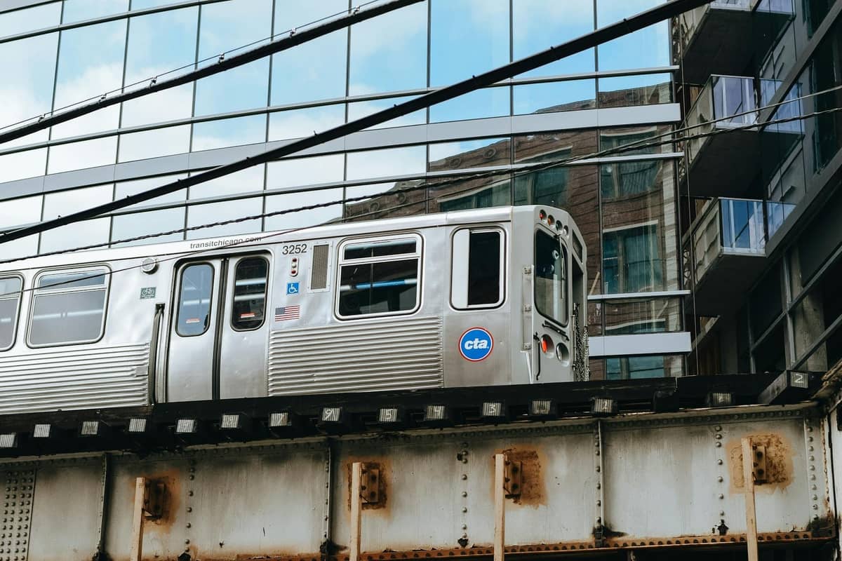 Erhöhter CTA-Zug auf Schienen vor einem modernen Glasgebäude in Chicago, der den erschwinglichen öffentlichen Nahverkehr in der Innenstadt zeigt.