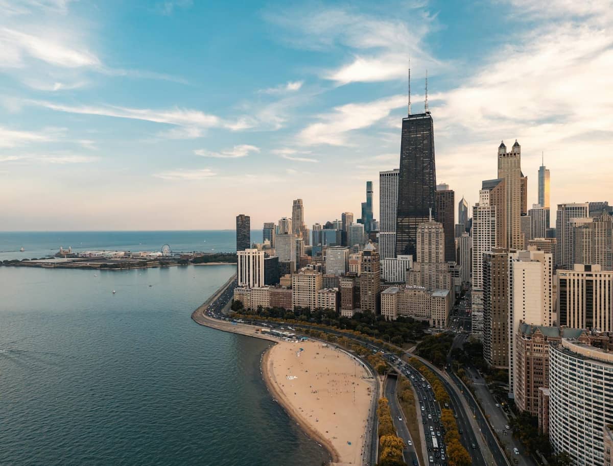 Seeblick auf die Skyline von Chicago mit Sandstrand und klarem Himmel, was auf angenehmes Wetter für Reisen außerhalb der Hauptsaison hindeutet.