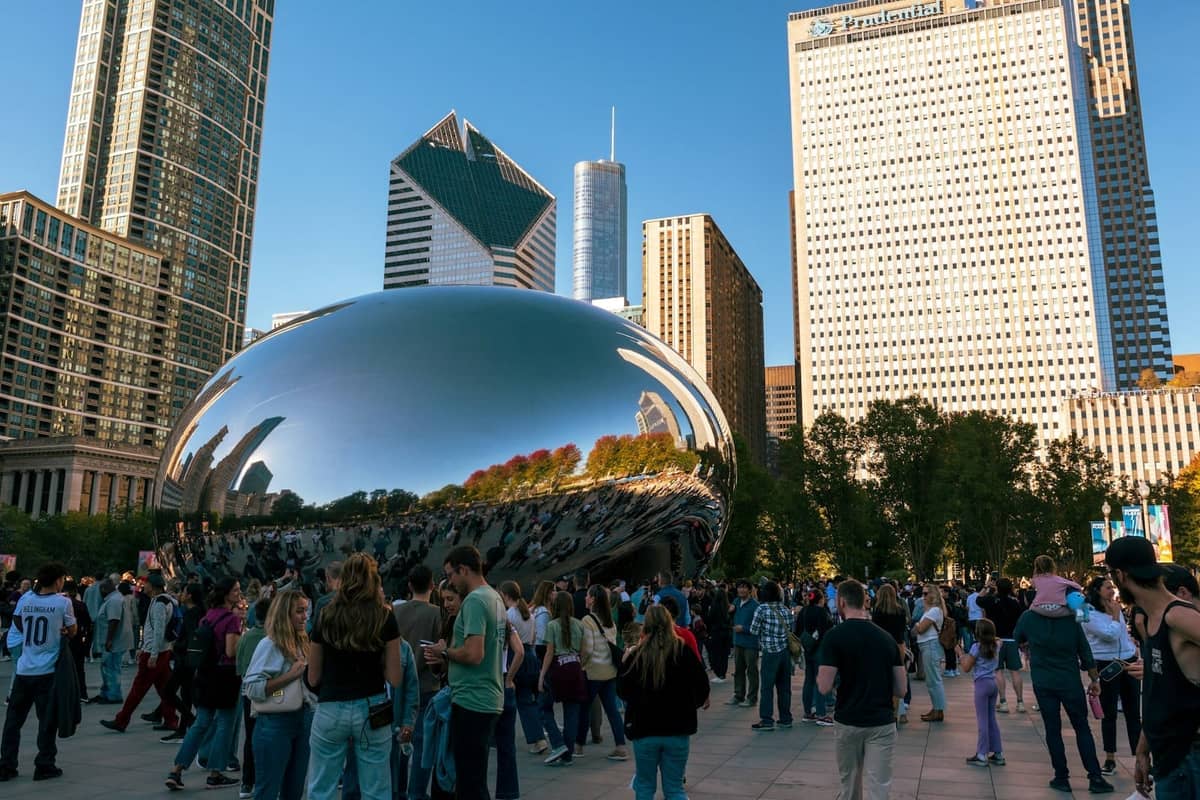 Multitudes de turistas reunidos alrededor de la escultura Cloud Gate de Chicago en Millennium Park con los rascacielos de la ciudad de fondo en un día soleado.