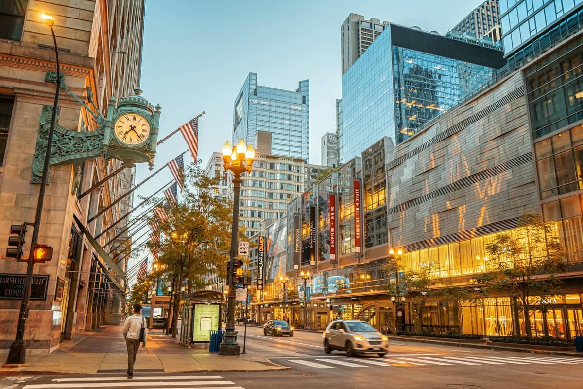 Die State Street in der Innenstadt von Chicago mit der Uhr von Marshall Field's, Macy's, Fahnen, modernen Glasgebäuden und einigen Menschen und Autos auf der Straße.