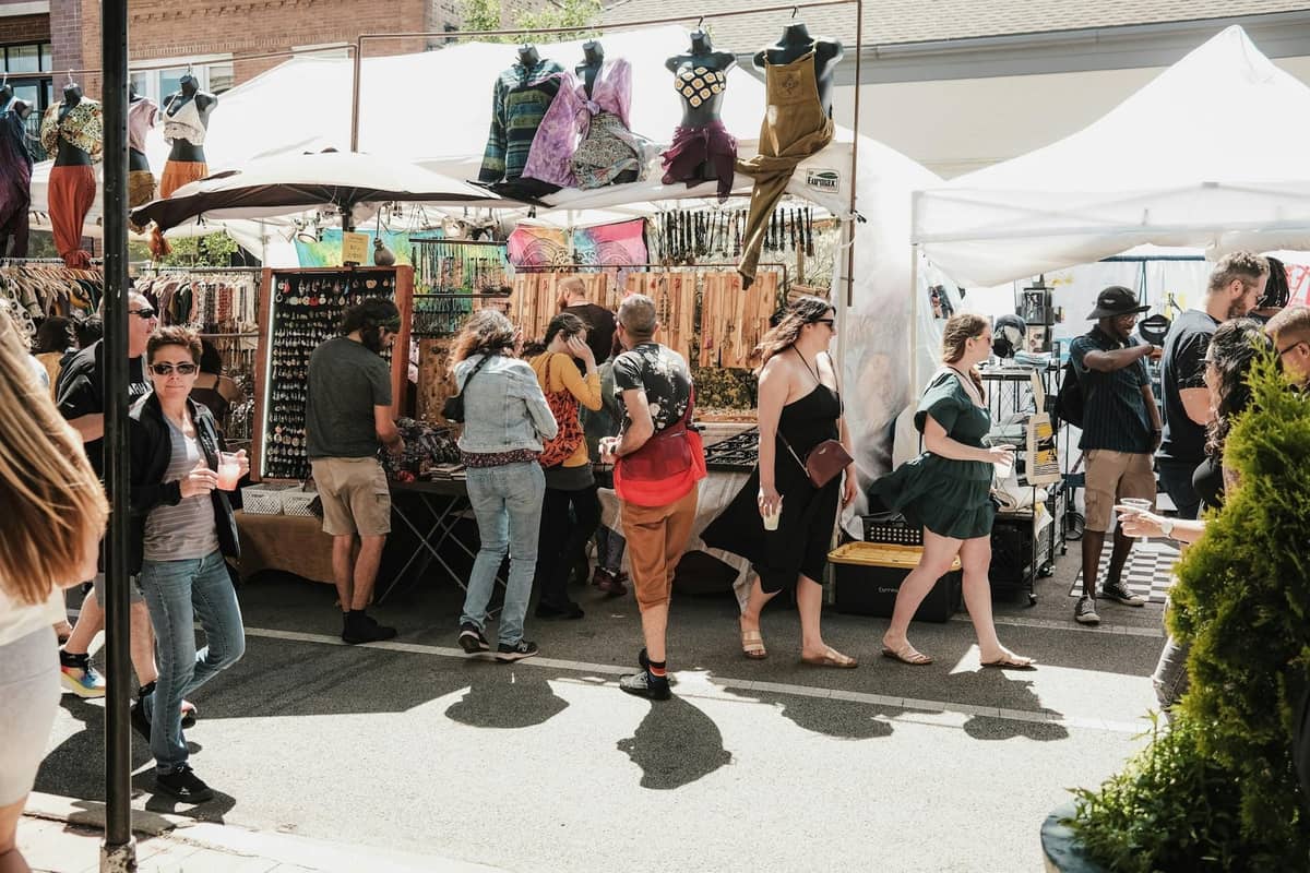 Freiluftmarkt in Chicago mit Menschen, die an Ständen mit Kleidung, Schmuck und Kunsthandwerk unter weißen Zelten an einem sonnigen Tag stöbern.
