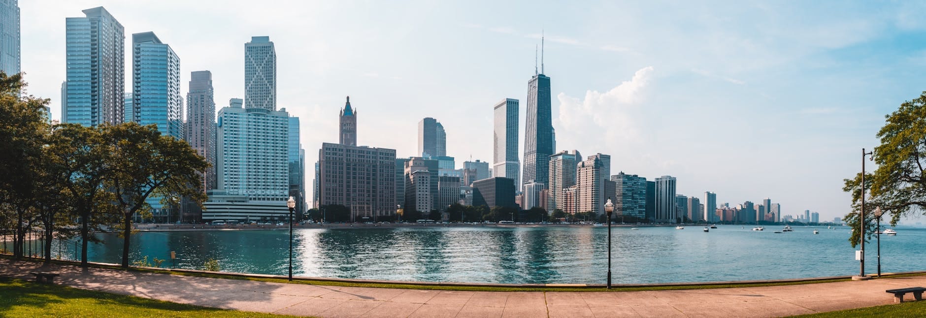 Vista panorâmica do skyline de Chicago a partir do parque à beira-lago em um dia ensolarado, com arranha-céus imponentes, céu azul e caminhos para caminhada à beira do lago.