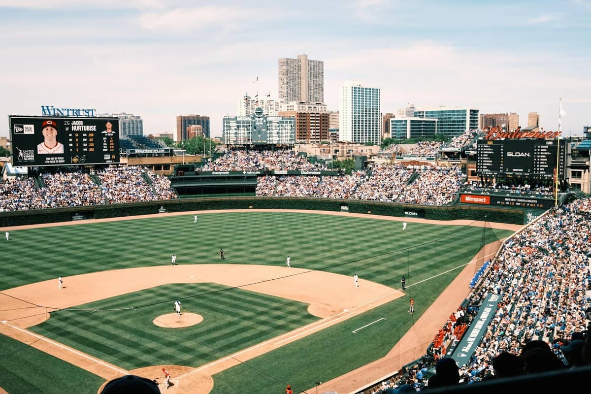 Una folla numerosa all'interno dello stadio di baseball Wrigley Field di Chicago che guarda una partita in una giornata di sole, con lo skyline della città visibile oltre il campo esterno.