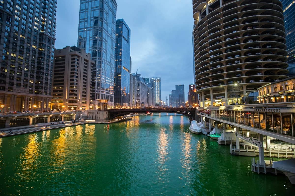 A view of the Chicago River dyed bright green for St. Patrick’s Day, surrounded by city buildings and bridges at dusk.