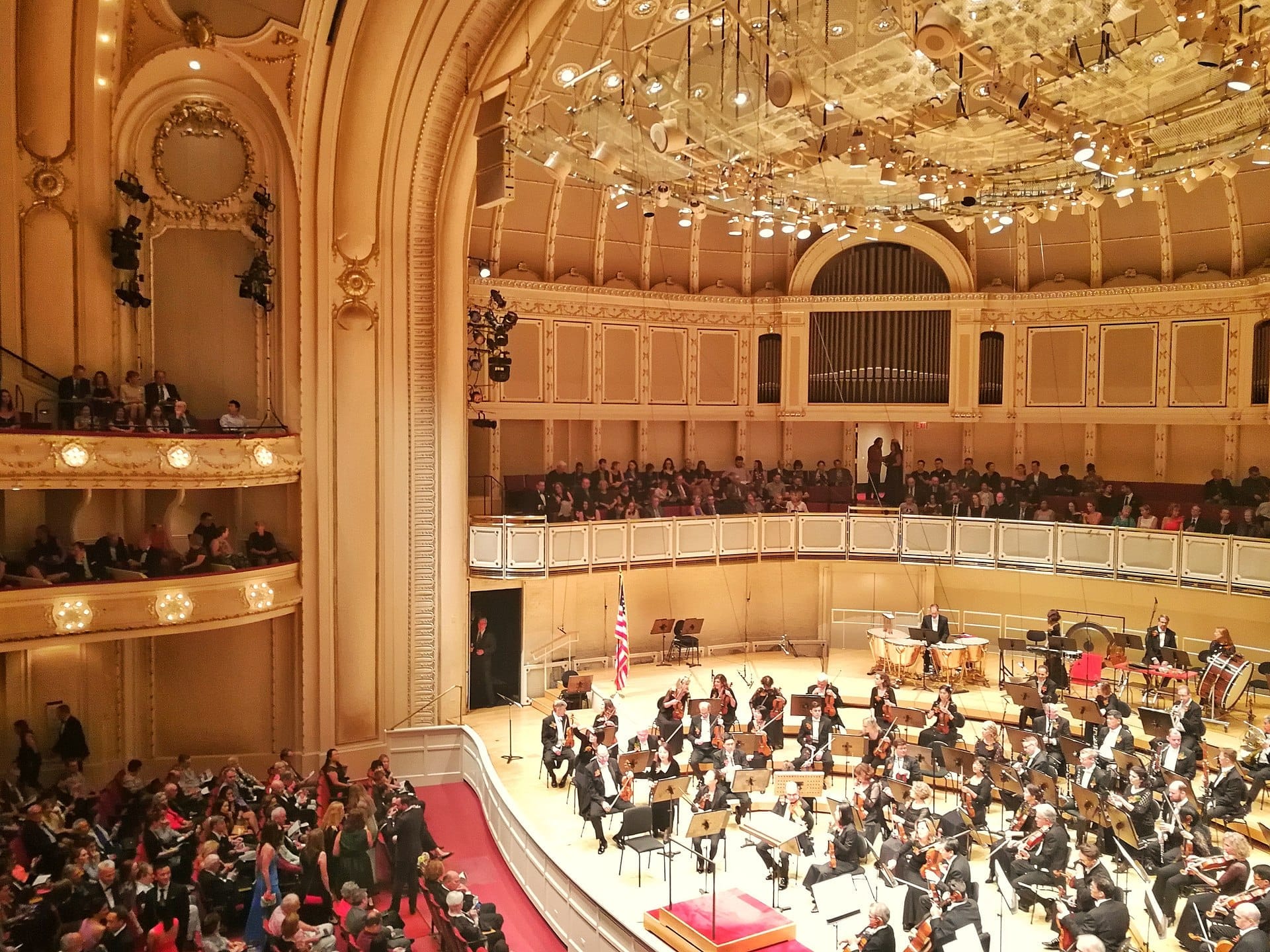 Orchestra che si esibisce sul palco del Chicago Symphony Center, circondata da un auditorium dorato, soffitti alti e un pubblico che riempie la sontuosa sala da concerto.