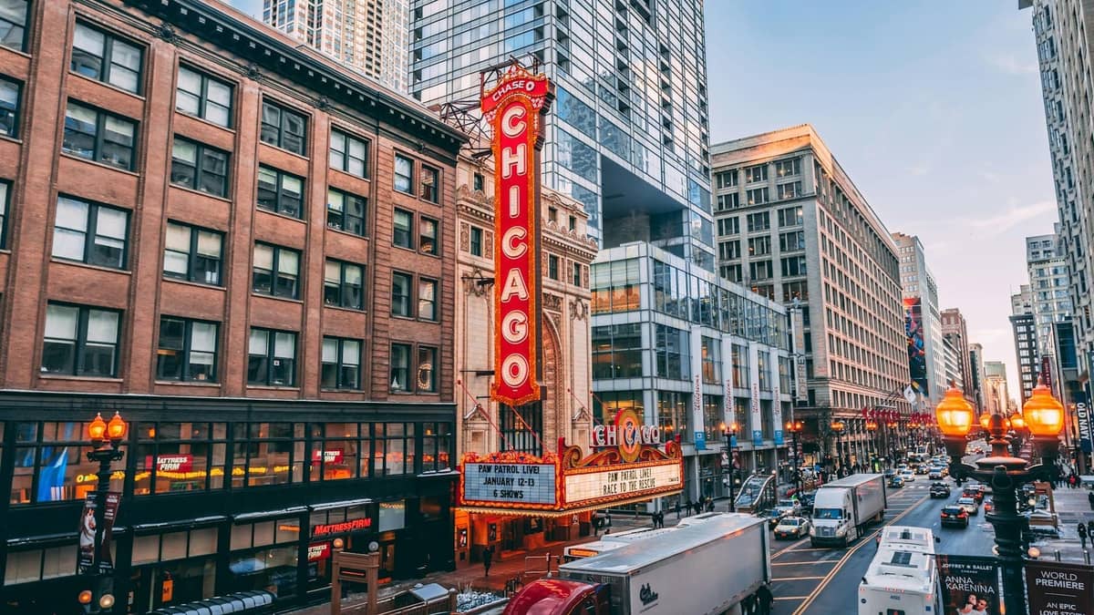El icónico Chicago Theatre con su marquesina roja y letrero vertical iluminado, rodeado de rascacielos del centro y el animado tráfico de la ciudad al atardecer.