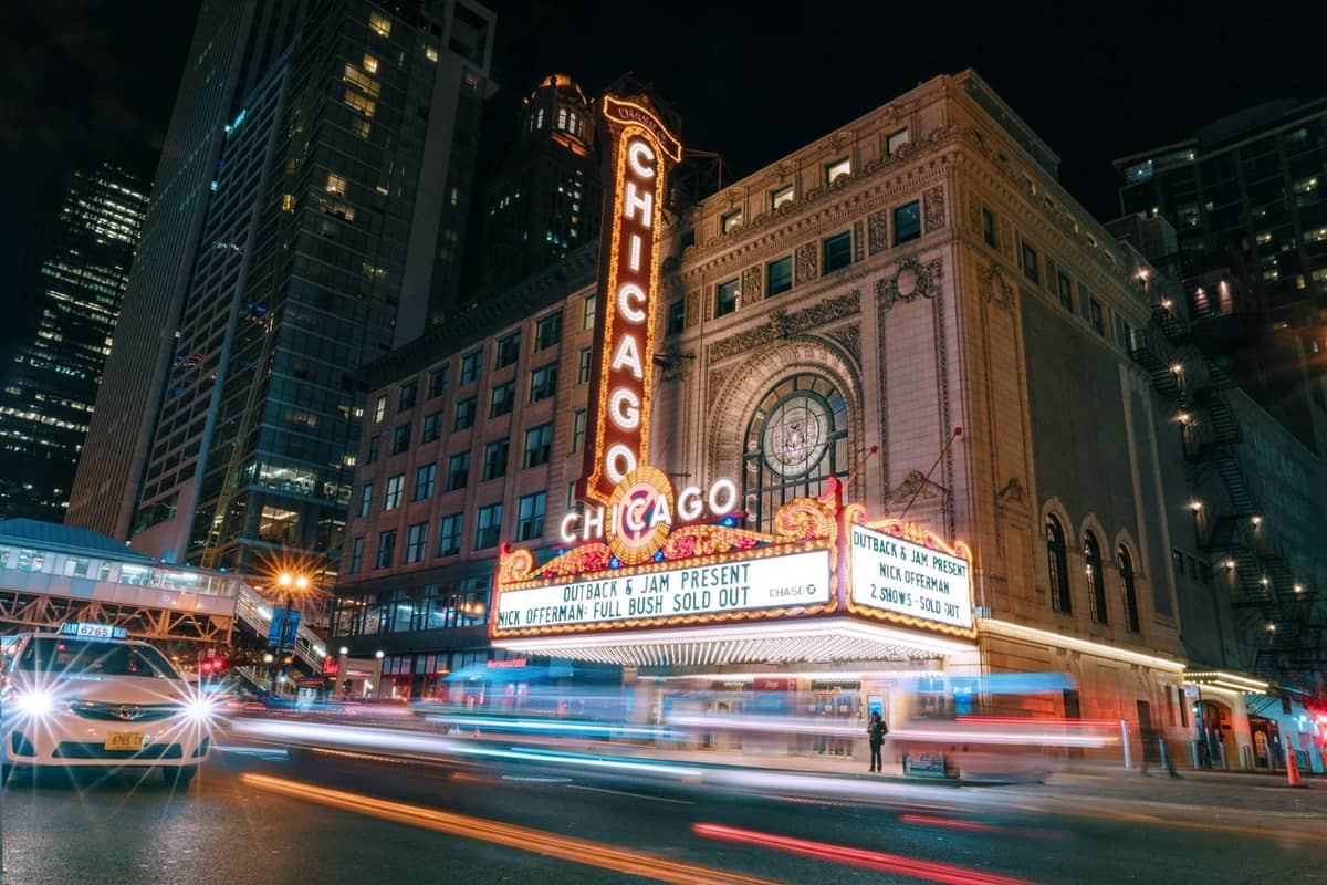 Vista nocturna del icónico marquesino del Chicago Theatre iluminado con los edificios del centro y el tráfico en el Loop.